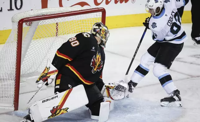 Utah Hockey Club's Logan Cooley, right, scores on Calgary Flames goalie Dan Vladar during the second period of an NHL hockey game in Calgary, Alberta, Thursday, Jan. 2, 2025. (Jeff McIntosh/The Canadian Press via AP)