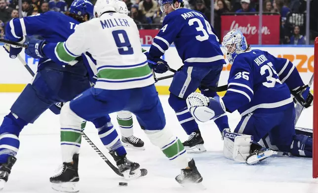 Toronto Maple Leafs goaltender Dennis Hildeby (35) looks on as Maple Leafs' Chris Tanev, left, and Vancouver Canucks' J.T. Miller (9) battle for the rebound during the first period of an NHL hockey game in Toronto, Saturday, Jan. 11, 2025. (Frank Gunn/The Canadian Press via AP)