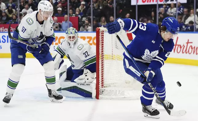Toronto Maple Leafs' Matthew Knies (23) controls a bouncing puck as Vancouver Canucks' Tyler Myers (57) and goaltender Kevin Lankinen (32) look on during second period NHL hockey action in Toronto on Saturday, January 11, 2025. (Frank Gunn/The Canadian Press via AP)