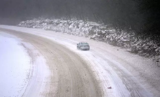 A car slowly navigates a snow-covered interstate Sunday, Jan. 5, 2025, in St. Louis. (AP Photo/Jeff Roberson)