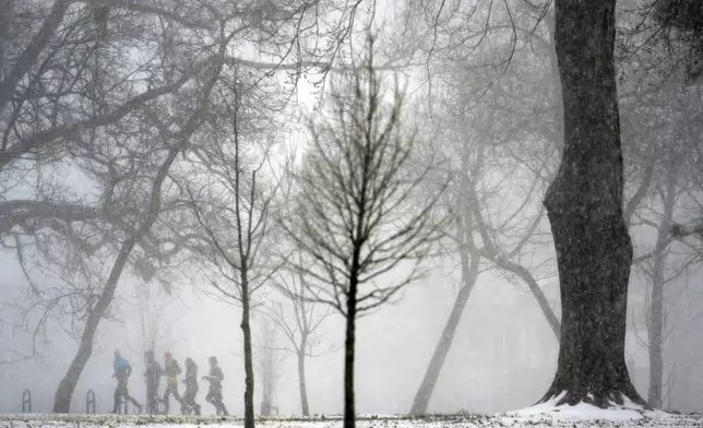 A group of people jog in the distance as heavy snow falls Sunday, Jan. 5, 2025, in St. Louis. (AP Photo/Jeff Roberson)