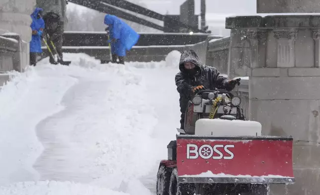 Workers clear snow from a walkway Sunday, Jan. 5, 2025, in St. Louis. (AP Photo/Jeff Roberson)