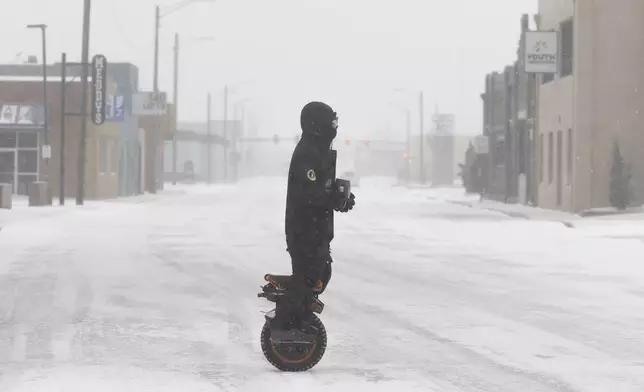 Brenden Campbell makes his way through downtown Wichita, Kan., on a one-wheel electric scooter during a severe winter storm on Sunday, Jan. 5, 2025. (Travis Heying/The Wichita Eagle via AP)