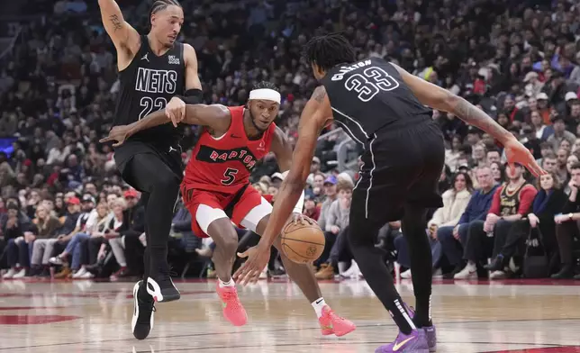 Toronto Raptors' Immanuel Quickley (5) drives between Brooklyn Nets' Jalen Wilson, left, and Nic Claxton (33) during the first half of an NBA basketball game in Toronto on Wednesday, Jan. 1, 2025. (Chris Young/The Canadian Press via AP)