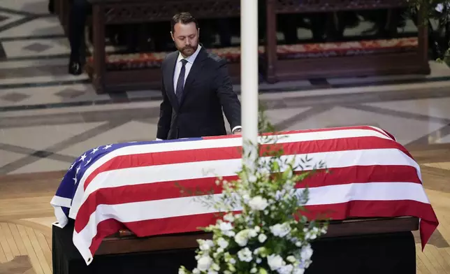 Grandson Jason Carter, walks by and touches the flag-draped casket of former President Jimmy Carter, after speaking a tribute at the state funeral for Carter at Washington National Cathedral, Thursday, Jan. 9, 2025, in Washington. (AP Photo/Ben Curtis)