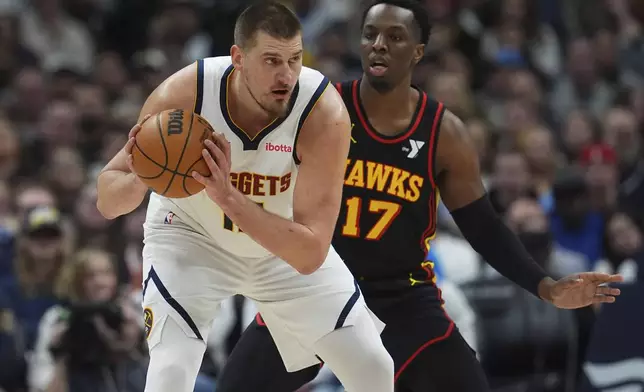 Denver Nuggets center Nikola Jokic, left, looks to pass the ball as Atlanta Hawks forward Onyeka Okongwu defends in the first half of an NBA basketball game Wednesday, Jan. 1, 2025, in Denver. (AP Photo/David Zalubowski)