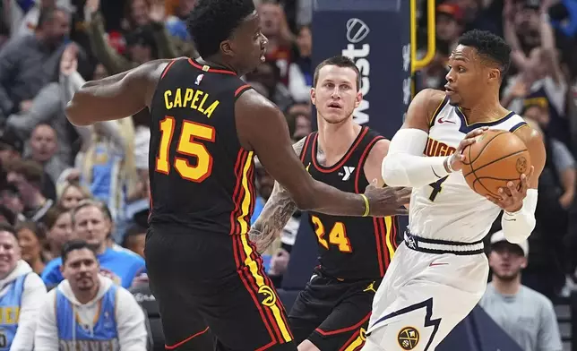 Denver Nuggets guard Russell Westbrook, right, drives to the basket as Atlanta Hawks center Clint Capela, left, and guard Garrison Mathews defend in the first half of an NBA basketball game Wednesday, Jan. 1, 2025, in Denver. (AP Photo/David Zalubowski)