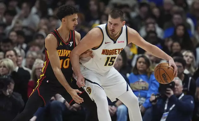 Denver Nuggets center Nikola Jokic, right, works the ball to the basket as Atlanta Hawks forward Zaccharie Risacher defends in the first half of an NBA basketball game Wednesday, Jan. 1, 2025, in Denver. (AP Photo/David Zalubowski)