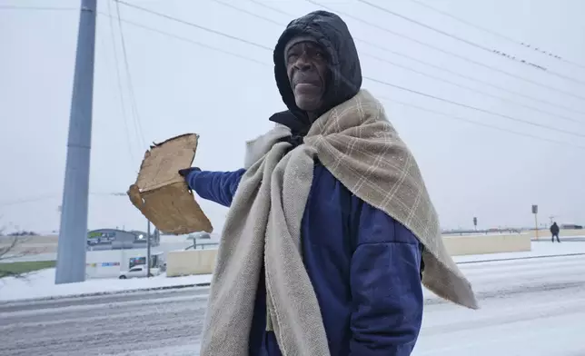 Frank Burnett, originally of Mississippi, uses a blanket to keep warm as he stands hoping for donations from passing motorists Thursday, Jan. 9, 2025, in Plano, Texas. (AP Photo/LM Otero)