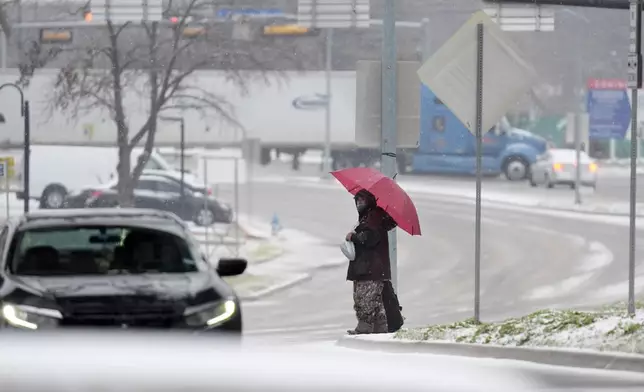 A man who gave his name as Servo uses an umbrella to cross a street as snow falls Thursday, Jan. 9, 2025, in Dallas. (AP Photo/LM Otero)