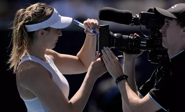 Paula Badosa of Spain autographs the screen on a television camera after defeating Marta Kostyuk of Ukraine in their third round match at the Australian Open tennis championship in Melbourne, Australia, Friday, Jan. 17, 2025. (AP Photo/Ng Han Guan)
