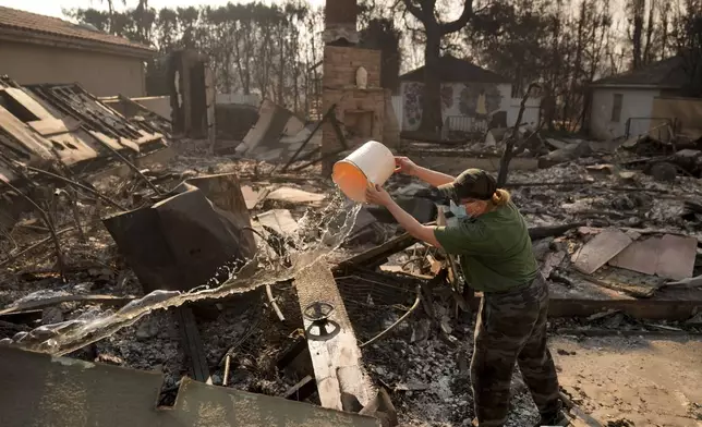 Nancy Belanger pours water on a neighbor's fire-ravaged property in the aftermath of the Palisades Fire in the Pacific Palisades neighborhood of Los Angeles, Thursday, Jan. 9, 2025. (AP Photo/Jae C. Hong)