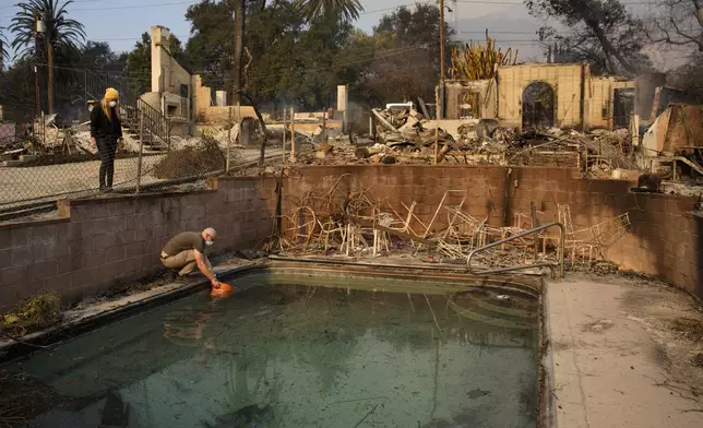 Robert Karban fills a bucket with water from a swimming pool to put out hot spots at a home destroyed by the Eaton fire, Thursday, Jan. 9, 2025, in Altadena, Calif. (AP Photo/John Locher)