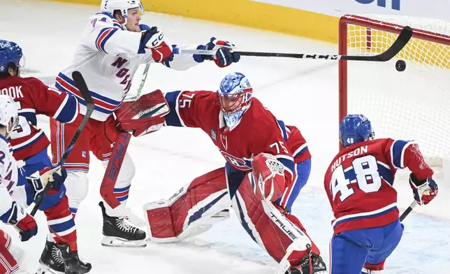 New York Rangers' Arthur Kaliyev (34) tries to knock the puck into the net behind Montreal Canadiens goaltender Jakub Dobes (75) as Canadiens' Lane Hutson defends during the first period of an NHL hockey game in Montreal, Sunday, Jan. 19, 2025. (Graham Hughes/The Canadian Press via AP)