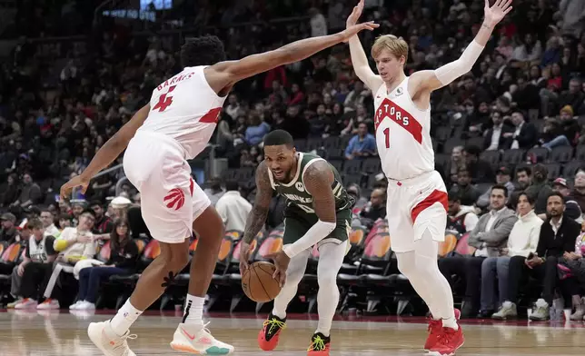 Milwaukee Bucks guard Damian Lillard (0) drives between Toronto Raptors forward Scottie Barnes (4) and Gradey Dick (1) during second-half NBA basketball game action in Toronto, Monday, Jan. 6, 2025. (Nathan Denette/The Canadian Press via AP)