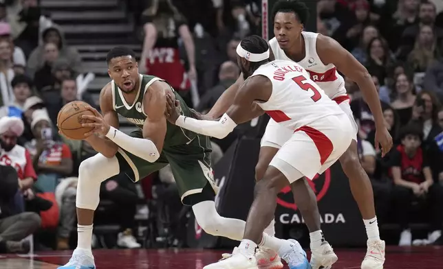 Milwaukee Bucks forward Giannis Antetokounmpo, left, looks to pass the ball while under pressure from Toronto Raptors guard Immanuel Quickley (5) and Scottie Barnes, right, during first-half NBA basketball game action in Toronto, Monday, Jan. 6, 2025. (Nathan Denette/The Canadian Press via AP)