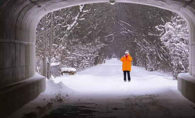 A walker pauses to take a photo as she walks along the snow-covered Monon Trail in Carmel, Ind., Monday, Jan. 6, 2025. (AP Photo/Michael Conroy)