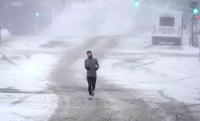 A person who declined to be identified jogs down a snow-covered street Sunday, Jan. 5, 2025, in St. Louis. (AP Photo/Jeff Roberson)