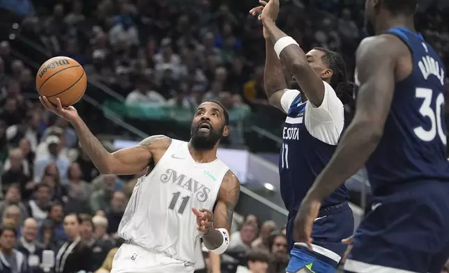 Dallas Mavericks guard Kyrie Irving (11) shoots again Minnesota Timberwolves center Naz Reid (11) and forward Julius Randle (30) during the second half of an NBA basketball game Wednesday, Jan. 22, 2025, in Dallas. (AP Photo/LM Otero)