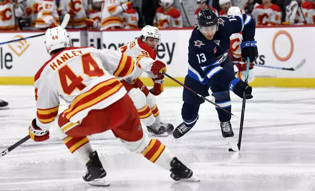 Winnipeg Jets' Gabriel Vilardi (13) carries the puck past Calgary Flames' Jakob Pelletier during the second period of an NHL hockey game in Winnipeg, Manitoba, Sunday, Jan. 26, 2025. (Fred Greenslade/The Canadian Press via AP)