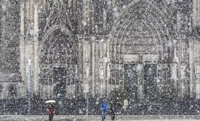 People walk in front of the Cologne Cathedral during heavy snowfall in Cologne, Germany, Thursday, Jan. 9, 2025. (AP Photo/Martin Meissner)