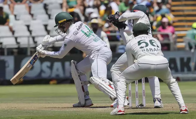 South Africa's Ryan Rickelton plays a shot while Pakistan's Mohammad Rizwan and Pakistan's Babar Azam look on during the second day of the second test match between South Africa and Pakistan in Cape Town, South Africa, Saturday, Jan. 4, 2025. (AP Photo/Halden Krog)