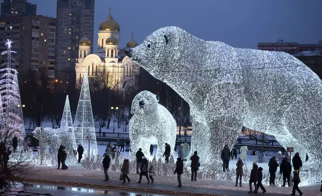 People walk and play at a park decorated for the New Year and Christmas festivities with an Orthodox Church in the background in Moscow, Russia, on Tuesday, Jan. 7, 2025. (AP Photo/Alexander Zemlianichenko)