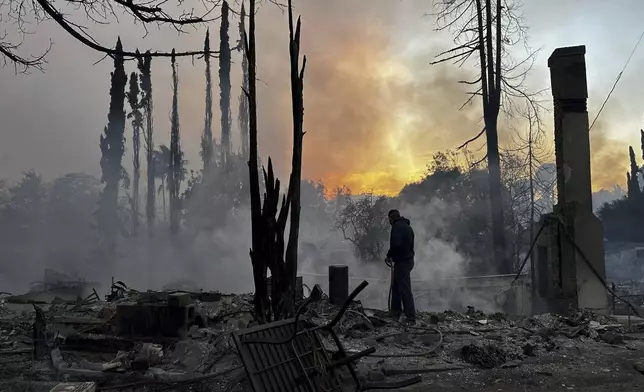 A resident hoses down hot spots in a fire-ravaged property after the Palisades Fire swept through in the Pacific Palisades neighborhood of Los Angeles, Wednesday, Jan. 8, 2025. (AP Photo/Eugene Garcia)