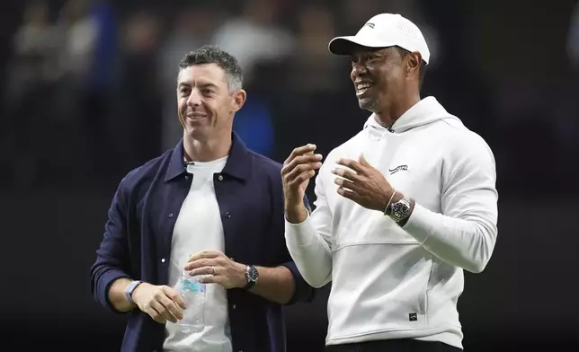 Rory McIlroy and Tiger Woods stand on the green as they watch New York Golf Club and The Bay Golf Club warmup for the inaugural match of the TMRW Golf League, Tuesday, Jan. 7, 2025, in Palm Beach Gardens, Fla. TGL features six teams of four players competing against each other in a tech-infused arena the size of a football field. (AP Photo/Rebecca Blackwell)