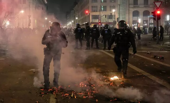 Police officers put out the fire in the streets after the fireworks for the New Year's celebrations in Berlin, Germany, Wednesday, Jan. 1, 2025. (AP Photo/Ebrahim Noroozi)