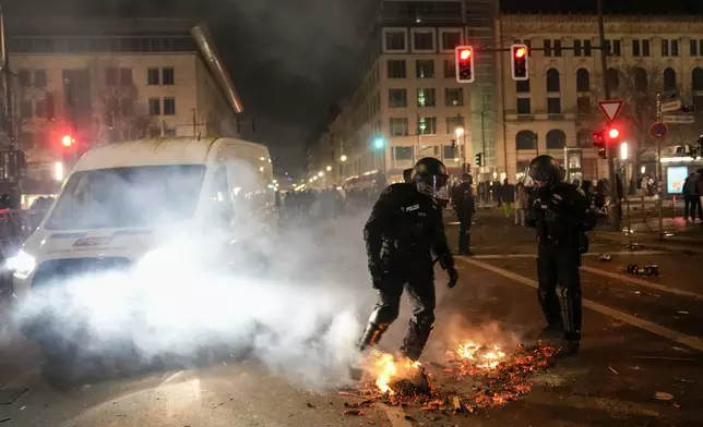 Police officers put out the fire in the streets after the fireworks for the New Year's celebrations in Berlin, Germany, Wednesday, Jan. 1, 2025. (AP Photo/Ebrahim Noroozi)