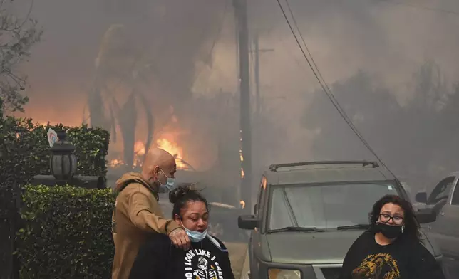 Residents embrace in front of burning structures as the Eaton Fire advances Wednesday, Jan. 8, 2025 in Altadena, Calif. (AP Photo/Nic Coury)