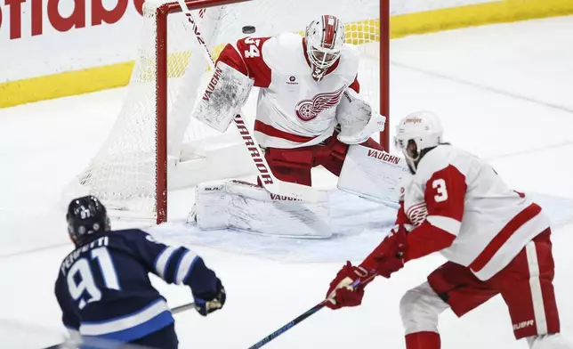 Detroit Red Wings goaltender Alex Lyon (34) saves a shot by Winnipeg Jets' Cole Perfetti (91) during first-period NHL hockey game action in Winnipeg, Manitoba, Saturday, Jan. 4, 2025. (John Woods/The Canadian Press via AP)