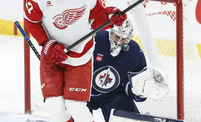 Winnipeg Jets goaltender Connor Hellebuyck, right, saves a tip by Detroit Red Wings' Michael Rasmussen (27) during first-period NHL hockey game action in Winnipeg, Manitoba, Saturday, Jan. 4, 2025. (John Woods/The Canadian Press via AP)