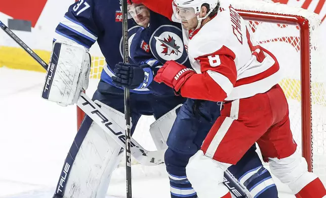 Winnipeg Jets' Neal Pionk, center, defends against Detroit Red Wings' Ben Chiarot (8) in front of Jets goaltender Connor Hellebuyck (37) during first-period NHL hockey game action in Winnipeg, Manitoba, Saturday, Jan. 4, 2025. (John Woods/The Canadian Press via AP)