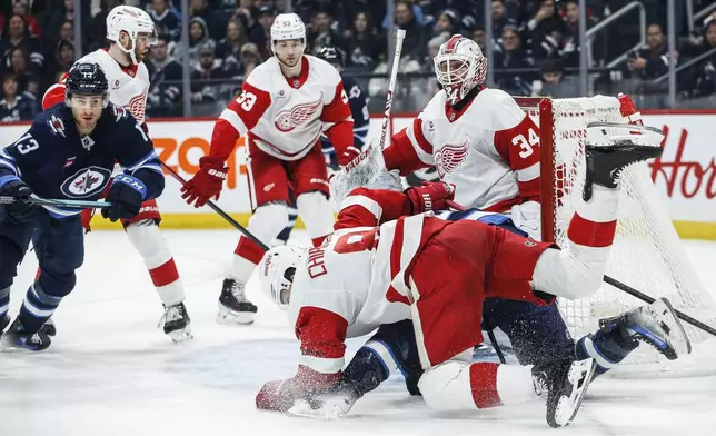 Detroit Red Wings' Ben Chiarot (8) defends against Winnipeg Jets' Mark Scheifele (55) in front of goaltender Alex Lyon (34) during second period NHL action in Winnipeg, Saturday, Jan. 4, 2025. (John Woods/The Canadian Press via AP)