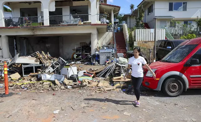 A woman walks in front of the home where a New Year's Eve fireworks explosion killed and injured people, Wednesday, Jan. 1, 2025, in Honolulu. (AP Photo/Marco Garcia)