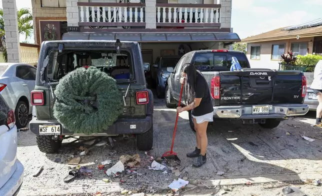 A woman sweeps debris from a driveway across the street from the home where a New Year's Eve fireworks explosion killed and injured people, Wednesday, Jan. 1, 2025, in Honolulu. (AP Photo/Marco Garcia)