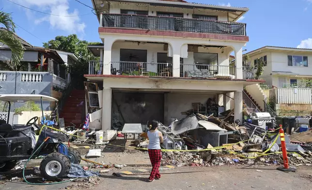 A woman stands in front of the home where a New Year's Eve fireworks explosion killed and injured people, Wednesday, Jan. 1, 2025, in Honolulu. (AP Photo/Marco Garcia)