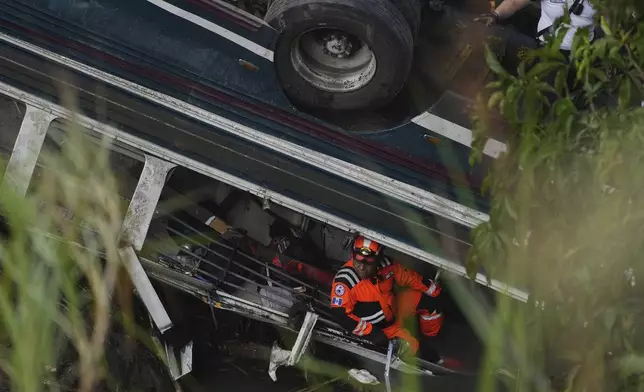 A firefighter works inside a bus that fell from a bridge, at the site of the fatal bus crash on the outskirts of Guatemala City, Monday, Feb. 10, 2025. (AP Photo/Moises Castillo)