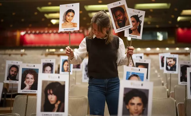 Publicist Abbie Gainher places placards with the images of actors on seats ahead of the BAFTA film awards in London, Wednesday, Feb. 12, 2024. (Photo by Scott A Garfitt/Invision/AP)
