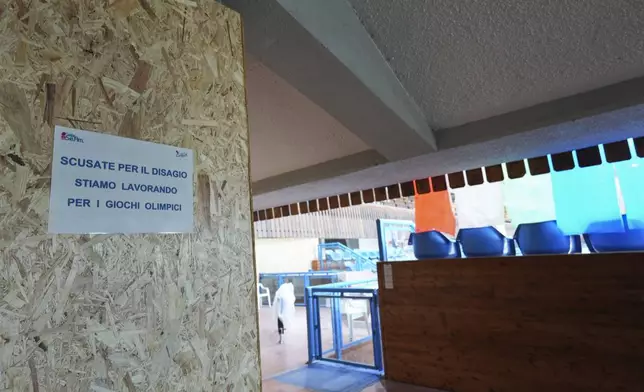 A sign with writing reading "Apologies for the inconvenience, we are working for the Olympic Games" is seen on a board inside the Stadio Olimpico del Ghiaccio, which will be called Cortina Curling Olympic Stadium, venue for the curling discipline at the Milan Cortina 2026 Winter Olympics, in Cortina d'Ampezzo, Italy, Thursday, Jan. 16, 2025. (AP Photo/Giovanni Auletta)
