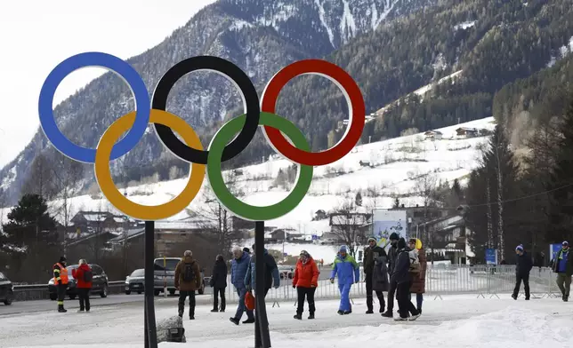 People walk near Olympic rings near the village of Anterselva where the Biathlon will take place during the Milan Cortina 2026 Winter Olympics, in northern Italy, Saturday, Jan. 25, 2025. (AP Photo/Alessandro Trovati)
