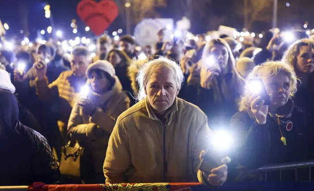 A man holds up his mobile phone light during a minute of silence ceremony as he protests over the collapse of a concrete canopy that killed 15 people more than two months ago, in Novi Sad, Serbia, Sunday, Feb. 2, 2025. (AP Photo/Armin Durgut)