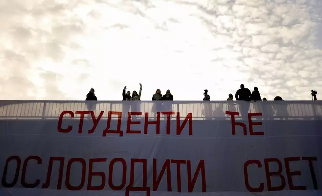 Students wave next to the banner reading "Students will set the World free" as they block the Bridge of Freedom and protest over the collapse of a concrete canopy that killed 15 people more than two months ago, in Novi Sad, Serbia, Sunday, Feb. 2, 2025. (AP Photo/Armin Durgut)