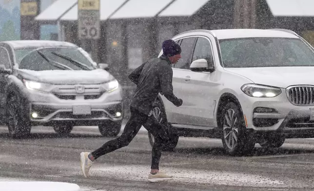A runner contends with a heavy snow while crossing Alameda Avenue at Marion Parkway as a winter storm sweeps over Colorado's Front Range communities Saturday, Feb. 15, 2025, in Denver. (AP Photo/David Zalubowski)