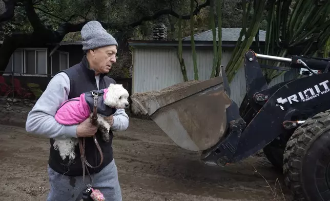 A residents carries their dog past a mud-covered street after a storm Friday, Feb. 14, 2025, in Sierra Madre, Calif. (AP Photo/Damian Dovarganes)