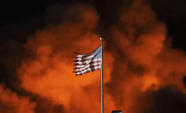 An American flag waves as flames engulf at SPS Technologies in Jenkintown, Pa., Monday, Feb. 17, 2025. (AP Photo/Matt Rourke)