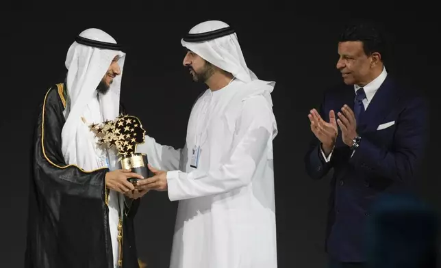 Saudi Arabian teacher Mansour bin Abdullah Al-Mansour, left, receives the Global Teacher Prize trophy from Dubai Crown Prince Sheikh Hamdan bin Mohammed Al Maktoum as Varkey foundation founder Sunny Varkey, right, applauds at a ceremony awarding the Global Teacher Prize in Dubai, United Arab Emirates, Thursday, Feb. 13, 2025. (AP Photo/Altaf Qadri)