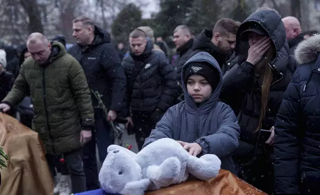 A boy puts a toy on a coffin as he says goodbye to Dmytro Yavorskyi, 37, Sofia Yavorska, 9, Olena Yavorska 38, who were killed on Feb. 1 by a Russian strike on residential building during a funeral ceremony in Poltava, Ukraine, Wednesday, Feb. 5, 2025. (AP Photo/Evgeniy Maloletka)